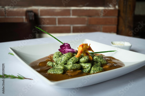 Spinach gnocchi with red sauce served with flowers on a white and rustic background