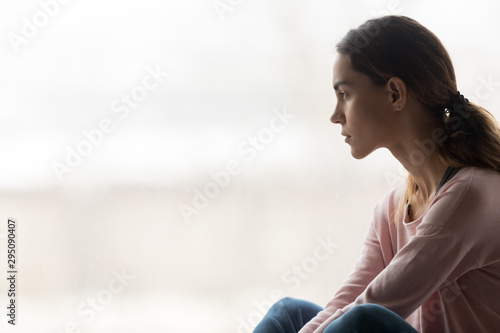 Thoughtful pensive girl sitting alone looking through window