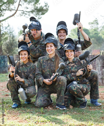 Portrait of joyous team of paintball players with marker guns outdoors