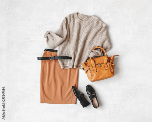 Brown midi pencil skirt, beige knitted oversize sweater, bag, belt, black loafers or flat shoes on grey background. Overhead view of women's casual day outfit. Flat lay, top view. Women clothes.