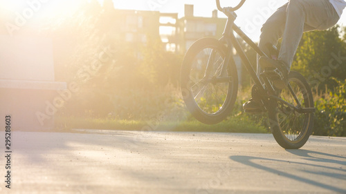 Close up of extreme young male riding manual wheelie trick on BMX bike on a beautiful summer afternoon