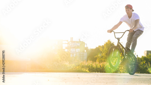 LENS FLARE Extreme young bmx biker riding manual wheelie trick in sunny park on beautiful summer day