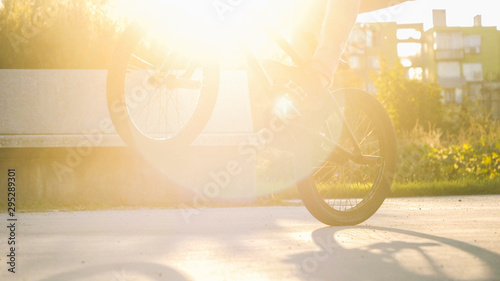 Close up of BMX biker riding manual wheelie trick in sunny park on beautiful summer day with lens flare