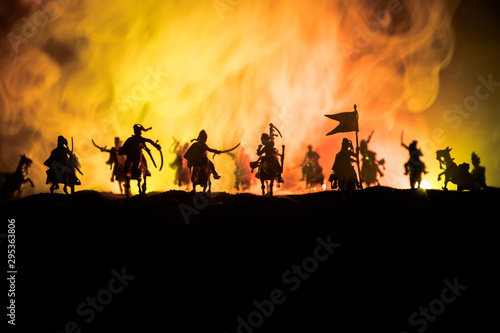 Medieval battle scene with cavalry and infantry. Silhouettes of figures as separate objects, fight between warriors on dark toned foggy background. Night scene.