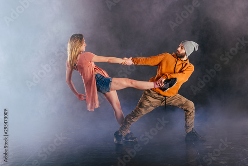 Couple dancing modern dance and showing off their leg stretch moves.Black background while the couple is dressed in urban colorful clothes...