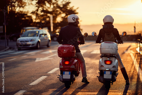 Couple riding motor scooter on road at sunset.