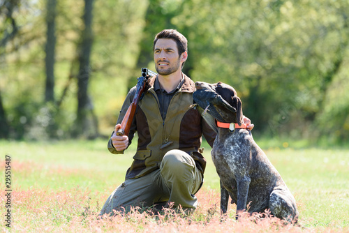 huntsman with gun kneeling by his dog