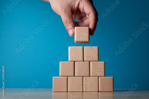 Hand arranging block on blue background. Business concept on progress or building something.