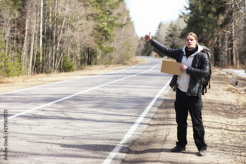 A young man is hitchhiking around the country. The man is trying to catch a passing car for traveling. The man with the backpack went hitchhiking to the south.