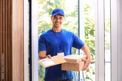 Young courier holding parcels on doorstep. Delivery service