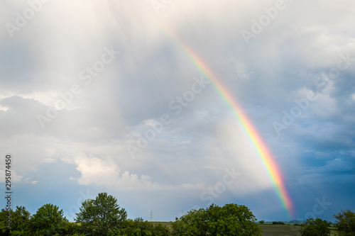 Rainbow over trees and agricultural fields with cloudy sky in background