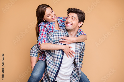 Photo of cheerful positive cute charming nice couple piggyback wearing checkered shirt jeans denim hugging man carrying his girl isolated over beige pastel color background
