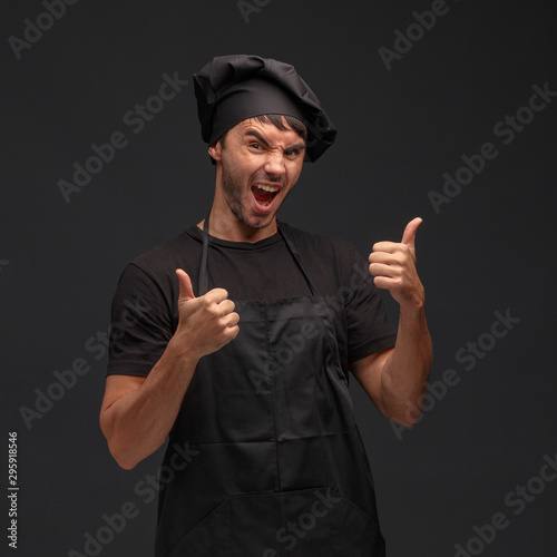 Young male cook in a black apron and hat.