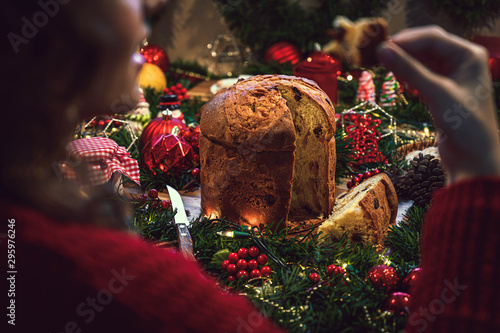 Young woman eating a piece of panettone, in the background a table of Christmas ingredients accompanied by hot chocolate, orange, cookies, cinnamon, pine.