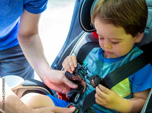 Toddler boy buckled into his car seat by his father