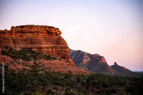 Row of red sandstone formations Capitol Butte glowing at sunset in Sedona, AZ with Coffee Pot Rock in distance