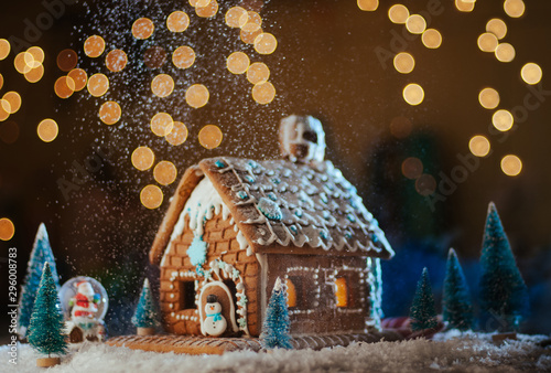 Traditional Christmas gingerbread house with snowfall on garland lights background