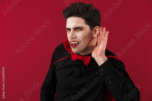 Image of vampire man in halloween costume listening with hand at his ear