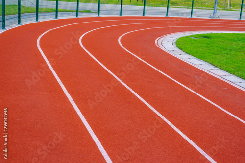Red running track or resin Emboss Topping with white lines in outdoor sport stadium, side is a field and park. Backgrounds and rubber texture.