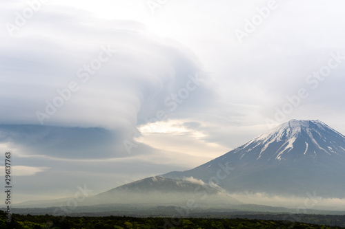 Mount Fuji before storm with cloudy hat on top , the light from sunset with dark clouds on overcast sky background, range of dark forest trees, beautiful landmark in Fujinomiya Shizuoka Japan.