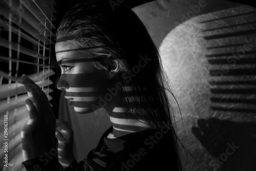 poster style Portrait of young woman looking through sun blinds window shutter artistic version 