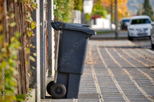 Black garbage bin for residual waste standing on the pavement in a residential area on a sunny autumn day in Germany