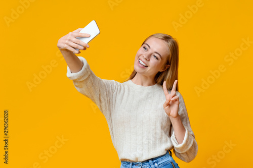 Smiling teenage girl taking selfie on smartphone, showing peace gesture