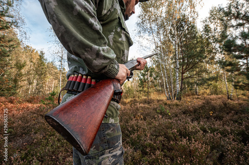 A hunter with a gun in his hands in hunting clothes in the autumn forest close-up. The hunting period, the fall season is open, the search for prey.