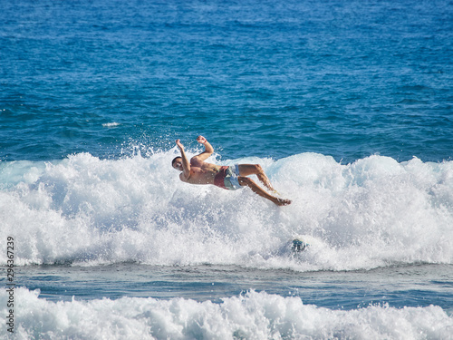 Surfer in wave wipes out and falls off surf board.