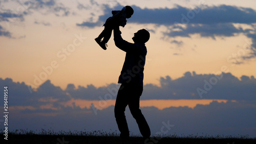 Father silhouette lifting up to sunset sky baby child with angel wings