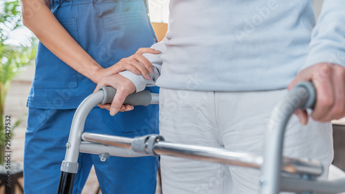 Cropped image of nurse helping senior woman to walk with walker at home