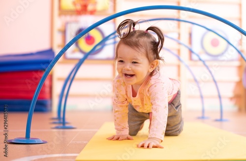 Baby toddler crawling on floor through tonnel in gym class. Lifestyle concept of children active games and exercises.