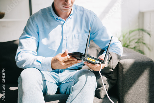 cropped view of businessman sitting on sofa and holding plugged router