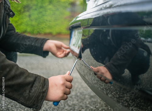 person steals the license plate on a car with a screwdriver