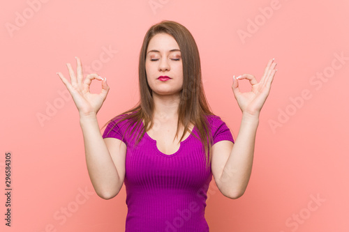 Young hispanic woman against a pink wall relaxes after hard working day, she is performing yoga.
