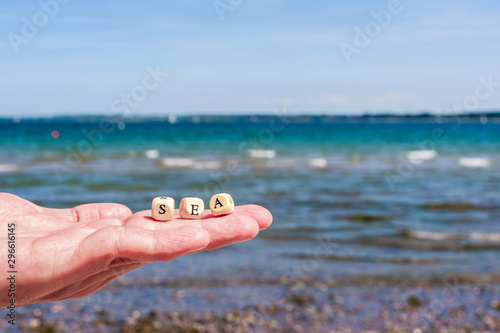 Hand with open palm on the background of the sea. The letters on the cubes are complex in the word SEA