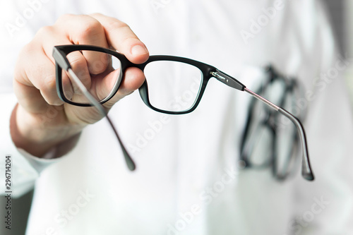 Optician giving new glasses to customer for testing and trying. Eye doctor showing patient lenses. Professional optometrist in white coat.