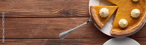 panoramic shot of delicious pumpkin pie with whipped cream on plate with spatula on brown wooden table