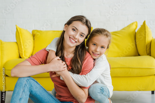 happy kid smiling while hugging cheerful babysitter in living room