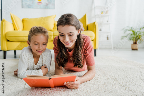 happy babysitter lying on carpet with cheerful kid while reading book