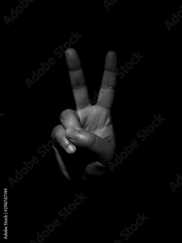 Low key black and white photo of a man showing two fingers indicating the number two or the victory sign