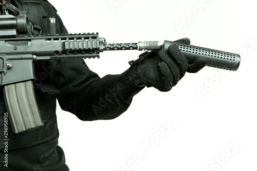 gloved hand of a man attaches a silencer to the barrel of an machine gun