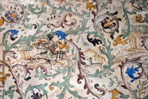 Fragment starożytnej ściany zamku. Na ścianie jest fresk. Obraz przedstawia polowanie.
