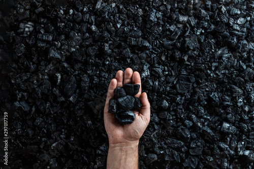 Male hand with coal on the background of a heap of coal, coal mining in an open pit quarry, copy space. Fossil fuels, environmental pollution.