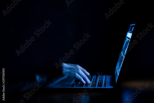 Hand of a man using laptop computer for hacking or steal data at night in office. Hacking concept