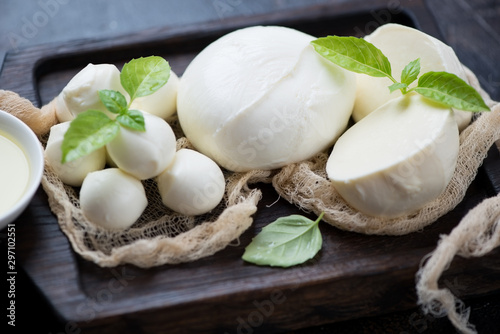 Close-up of various types of mozzarella cheese with fresh green basil on a black wooden serving tray