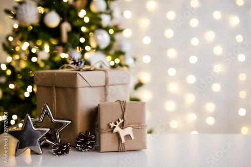 christmas and new year background - gift boxes and stars near decorated christmas tree and copy space over white wall with lights