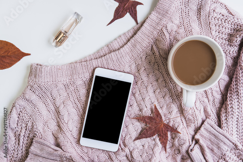 Empty screen smartphone with cup of coffee and dried autumn leaves and sweater, Top view