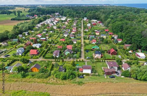 Aerial perspective drone view on allotment gardens with high density of houses in forest, sea and agricultural fields surroundings