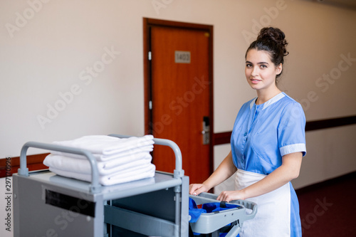 Chamber maid pulling cart with clean towels while moving along corridor in hotel